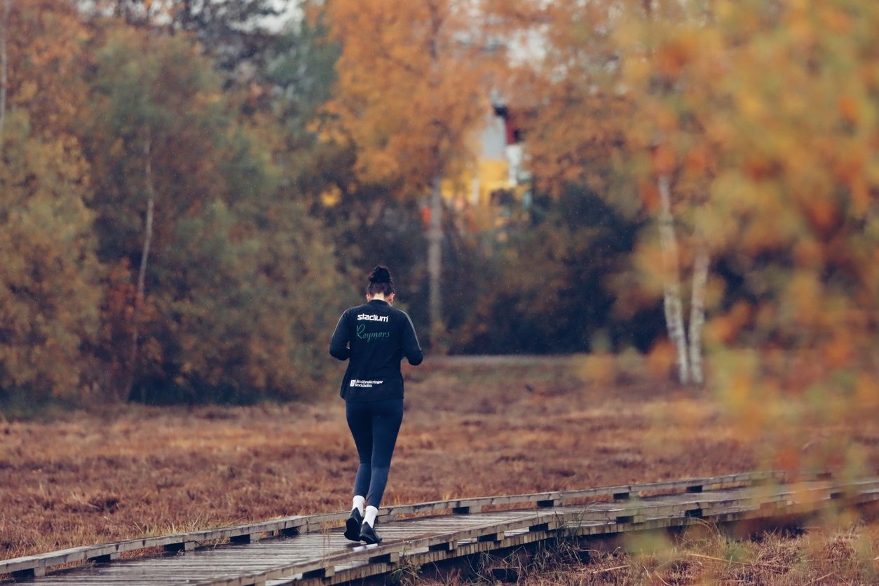 Runner jogging along a wooden boardwalk trail surrounded by bright autumn foliage